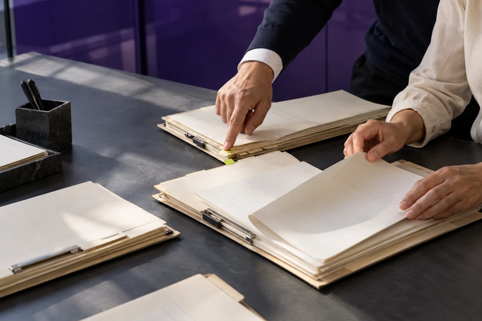 Illustrative scene: Hands reviewing paper folios at a violet-accented worktable